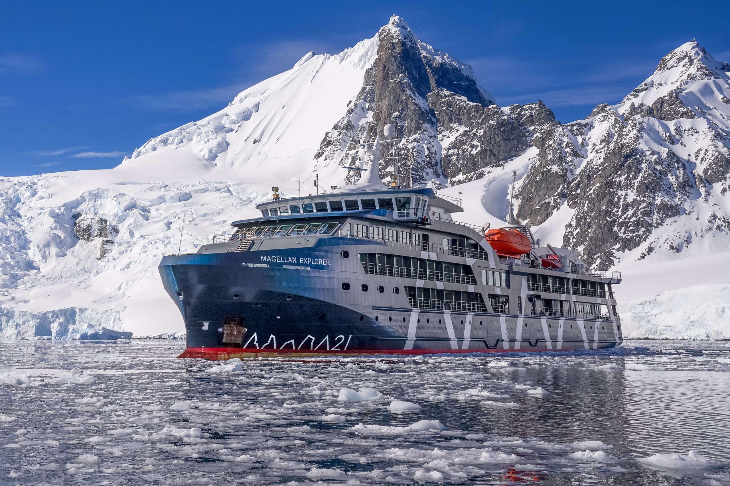 The ship Magellan Explorer in ice filled waters with mountain peaks in the background.