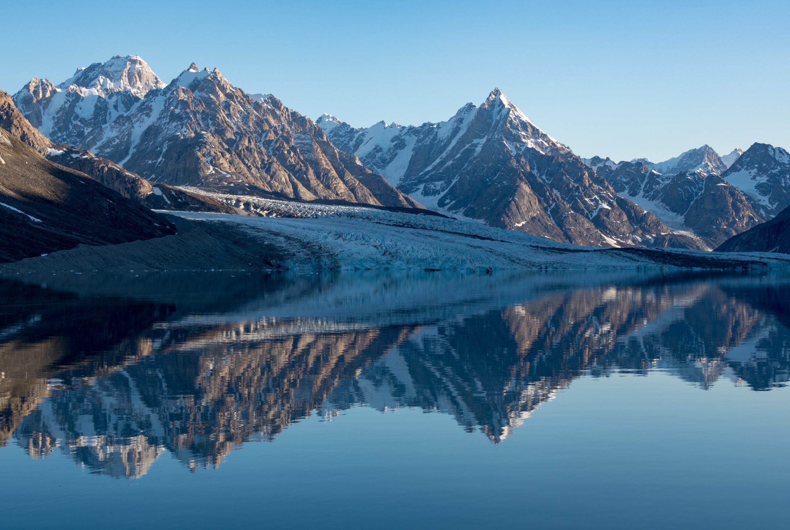 Mountains and a large glacier reflecting off still water.