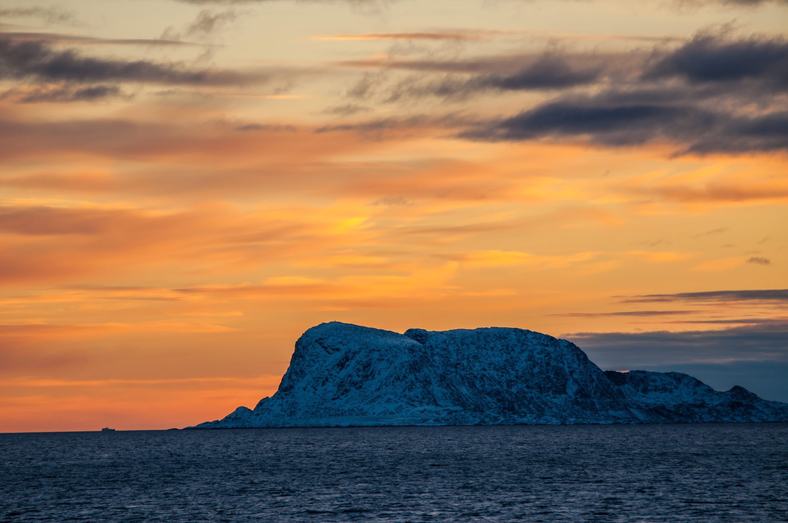 An orange sky with rocky island at sunset.