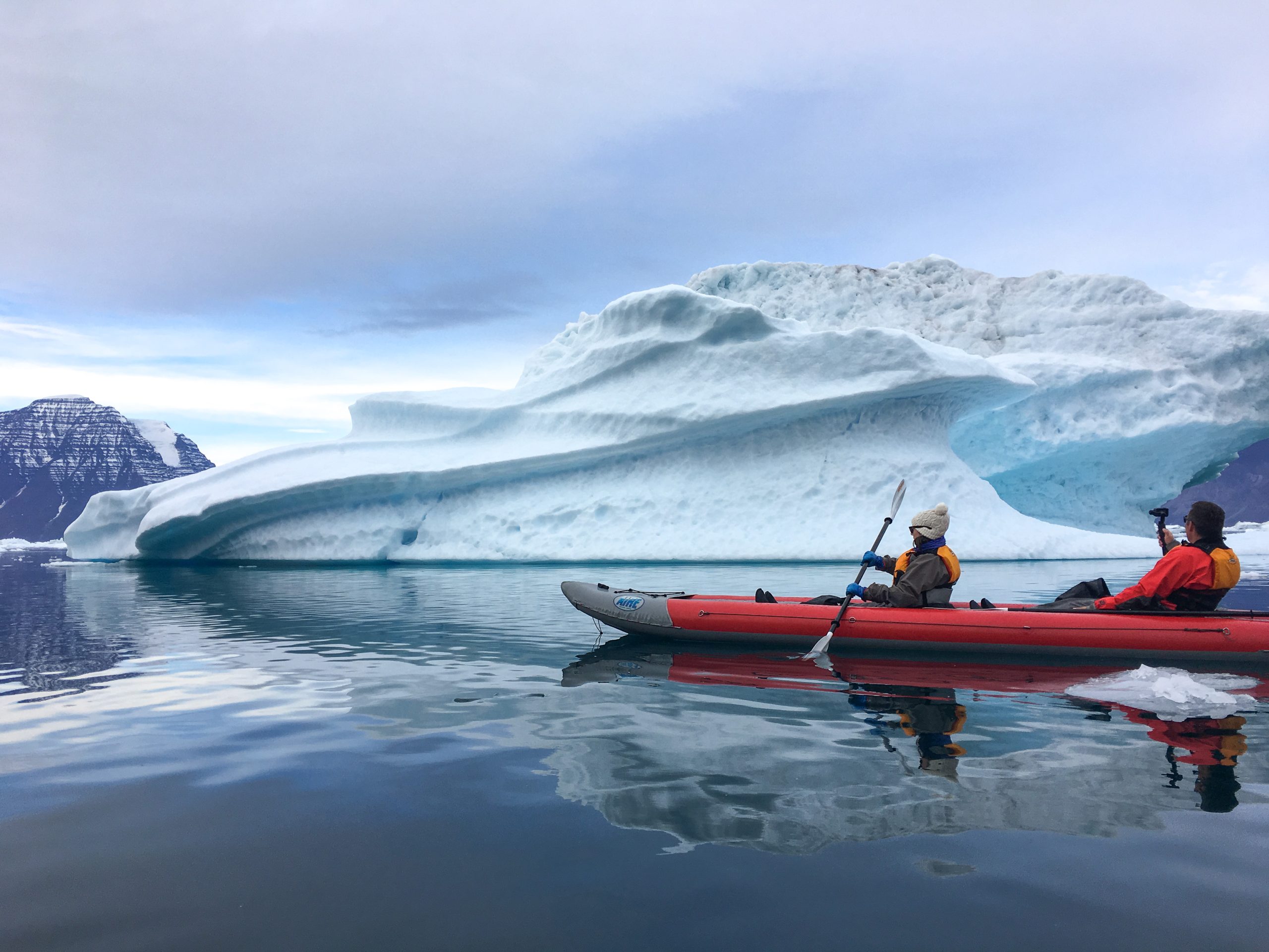Kayakers paddling past iceberg in East Greenland.