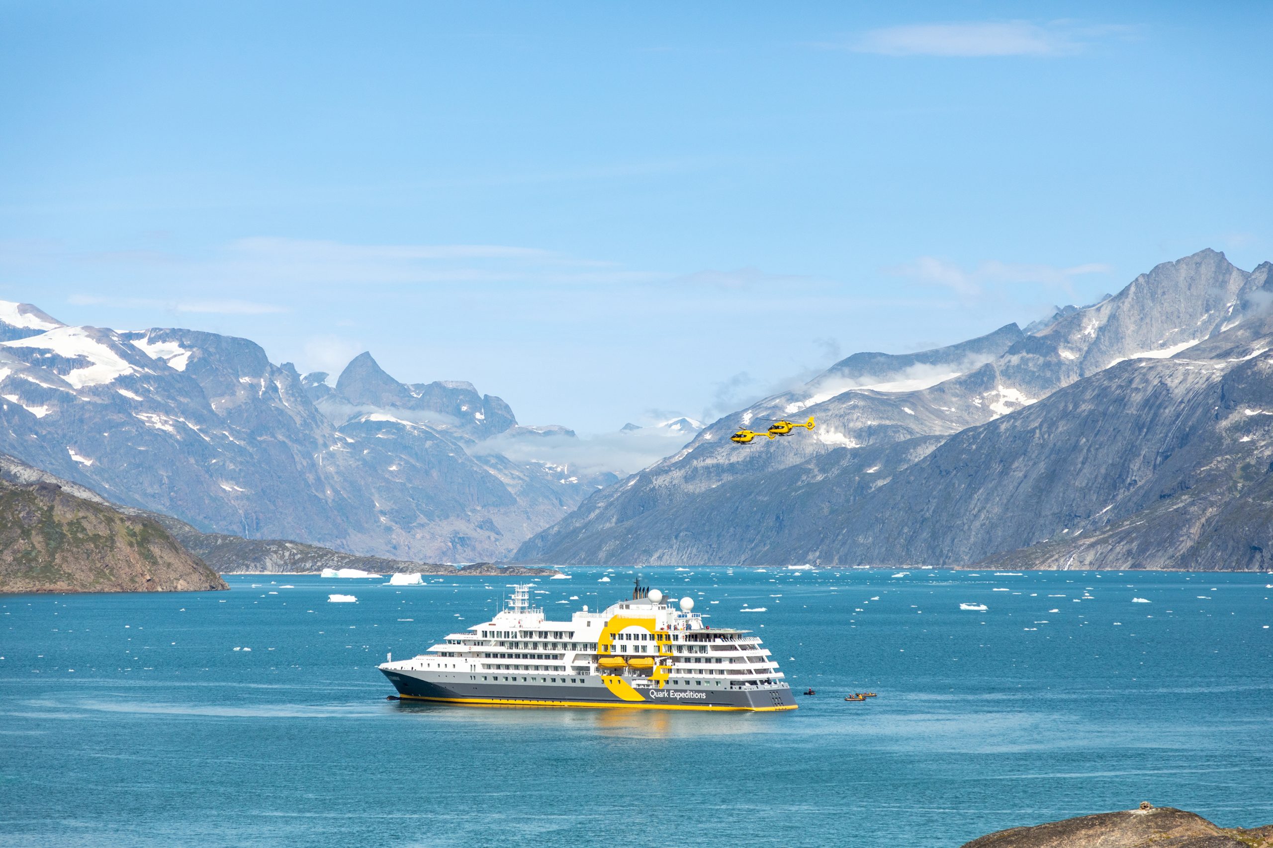 The ship Ultramarine in stunning fjord with helicopters flying nearby.