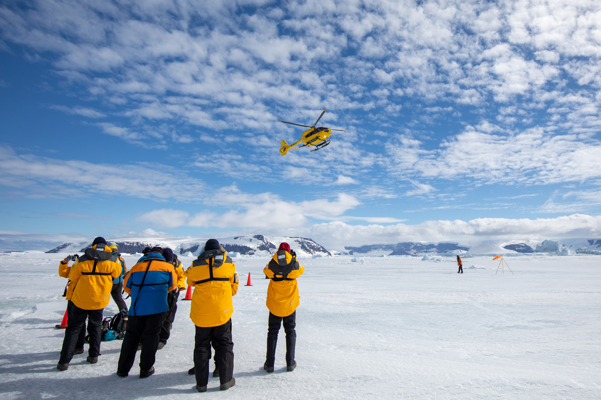 Guests standing on the ice with helicopter in the sky.